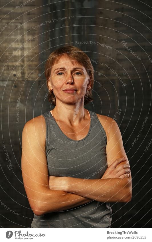 Close up front upper body portrait of one middle age athletic woman in sportswear in gym over dark background, looking at camera and smiling Lifestyle Sports