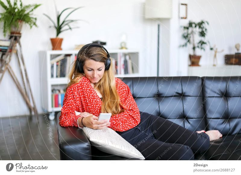 Young woman using an smartphone and listening music while lying on a leather couch Lifestyle Joy Happy Beautiful Hair and hairstyles Relaxation Calm