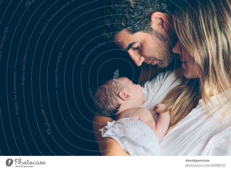 Couple embracing and looking to their newborn over dark background Lifestyle Happy Beautiful Child Human being Baby Toddler Woman Adults Man Parents Mother