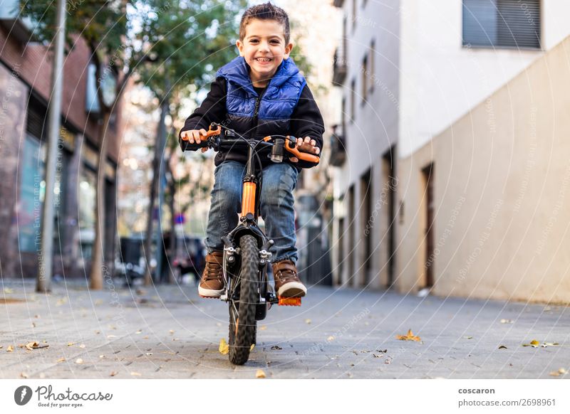 Little kid riding his bicycle on city street Lifestyle Joy Happy Beautiful Face Relaxation Leisure and hobbies Playing Children's game Summer Sun Sports Success