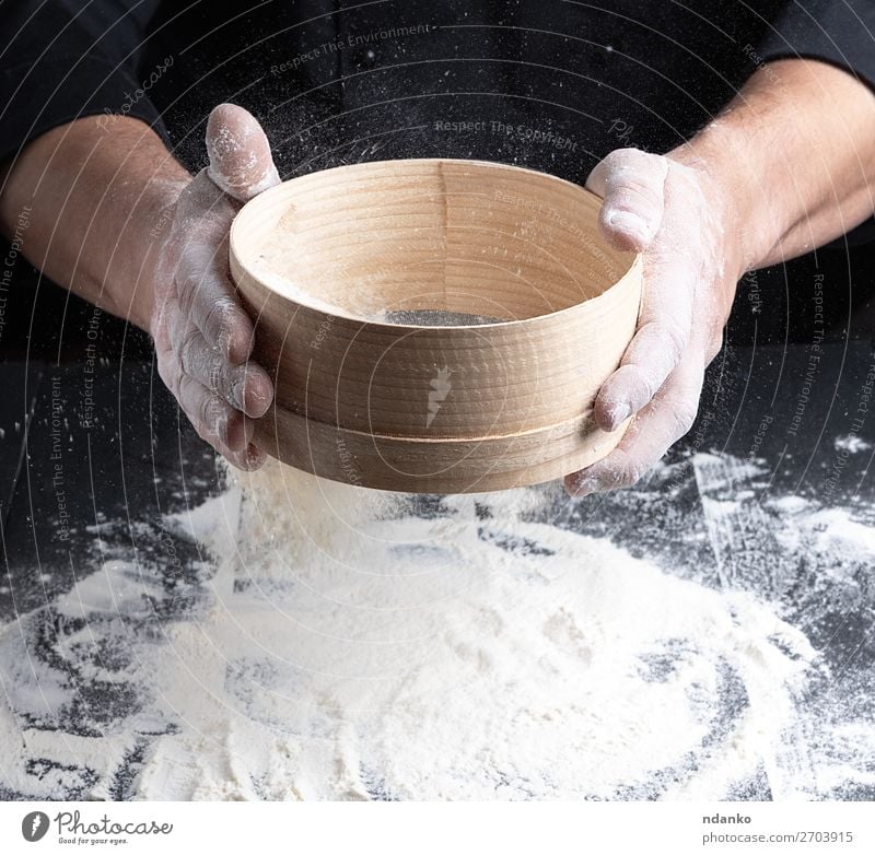 Chef in a black uniform holds in his hand a sieve Dough Baked goods Bread Nutrition Table Kitchen Human being Man Adults Hand Sieve Wood Movement Make Fresh