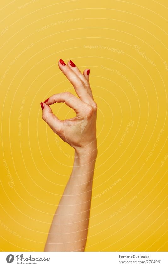 Hand signal for okay against a yellow background Feminine 1 Human being Sign Communicate OK Gesture Fingers Underarm Yellow Red Nail polish right-handed