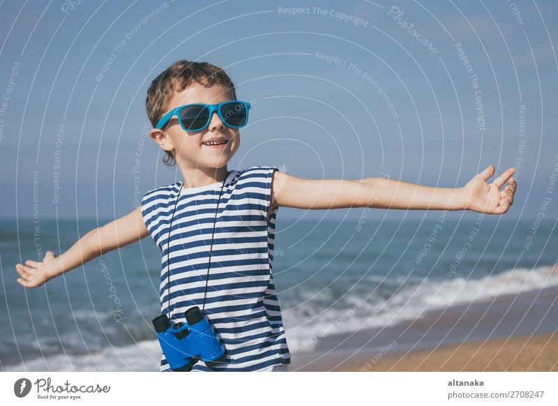 One happy little boy playing on the beach at the day time. He are dressed in sailor's vest. Kid having fun outdoors. Concept of sailor on vacation. Lifestyle