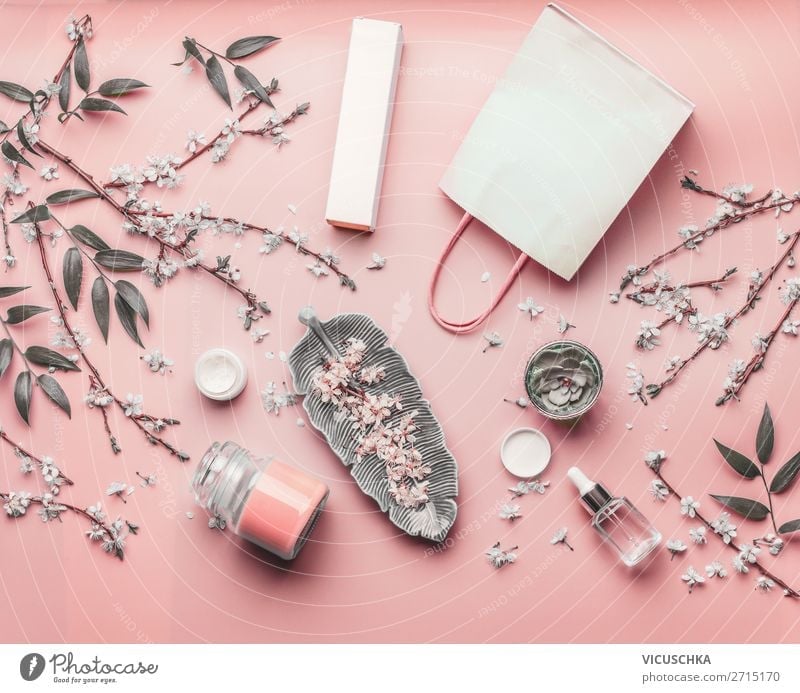 Cosmetic concept. Various facial products and paper shopping bag on pastel pink background with cherry blossom and leaves, top view, frame. Copy space for your design. Beauty blog layout. Flat lay