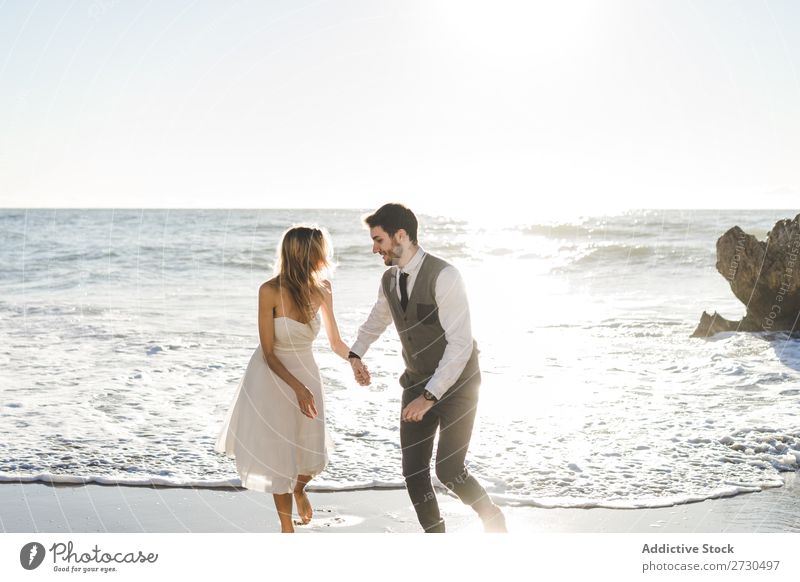 Beautiful bridal couple running on shore Couple Running Beach Happiness seaside holding hands Cheerful Exterior shot Together Contentment Summer Dress Wedding