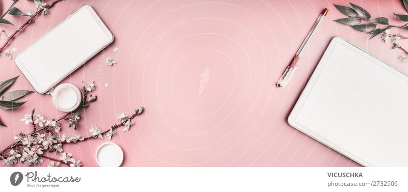Smartphone and tablet pc mock up on pastel pink desktop background with cosmetic, stationery supples and white blossom branches, top view. Beaut blog and female business concept. Flat lay, banner