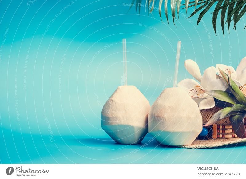 Fresh tropical coconut cocktail with drinking straws and palm leaves and flowers standing on blue turquoise background. Summer tropical vacation,travel and holiday concept
