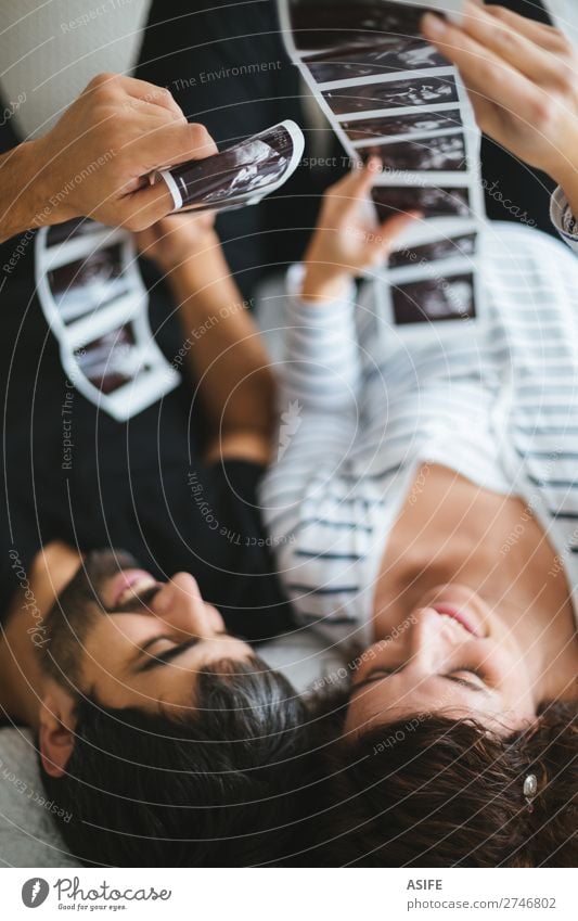 Happy and excited pregnant couple looking at the ultrasound images of their baby lying on the bed Beautiful Life Baby Woman Adults Man Parents Mother Father