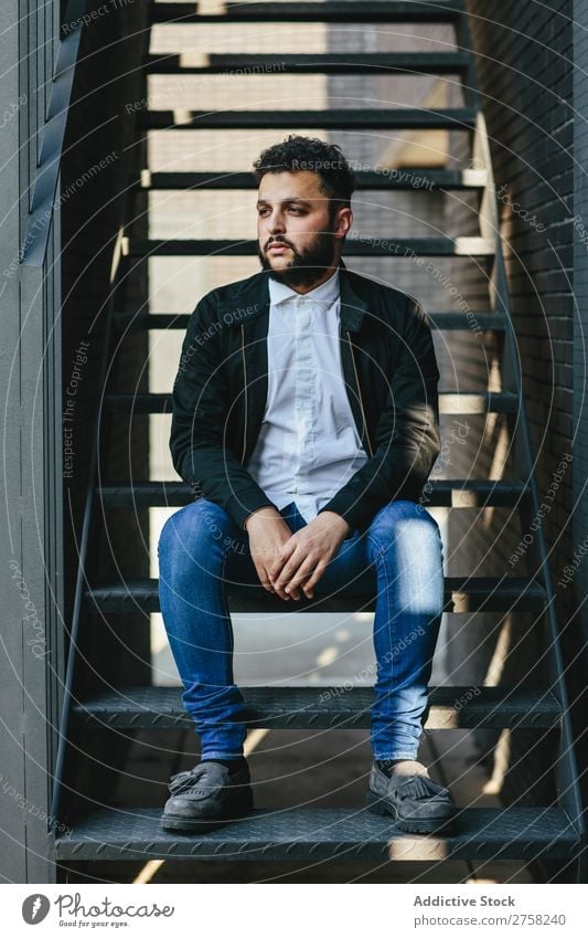 Thoughtful man sitting on stairs stylish pensive thoughtful looking at camera confident young cool person portrait modern model fashionable male serious casual