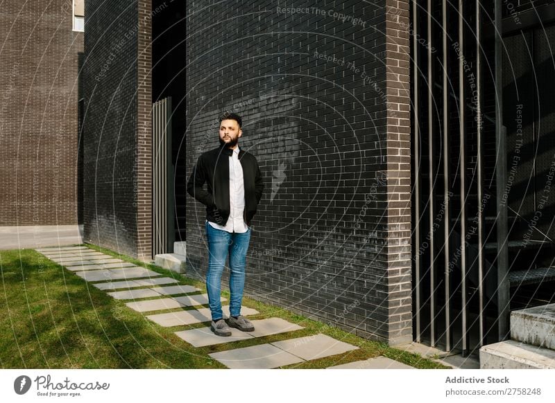 Trendy young man walking in the street looking away thoughtful pensive stylish brick wall standing confident cool person portrait modern model fashionable male