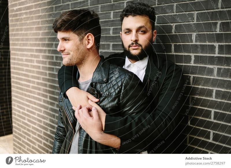 Gay couple hugging near brick wall gay embrace looking at camera happy standing posing homosexual pair male love two together lifestyle relationship young men