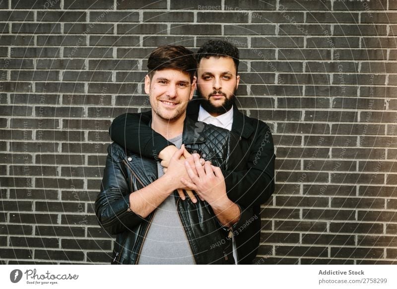 Gay pair hugging near brick wall Couple Homosexual Embrace Looking into the camera Happy Stand Wall (building) Brick Posture In pairs Man Love 2 Together