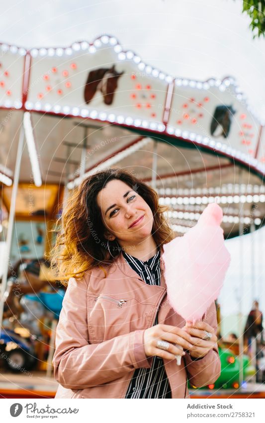 Smiling female holding a cotton candy near the merry-go-round. woman park person pink pretty sweet food eat sugar fun lifestyle portrait young smile snack