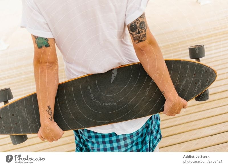 Man with tattoos holding skateboard at shore. Back view. Skateboard Coast Beach Leisure and hobbies Multicoloured youngster Action Youth (Young adults) Sports