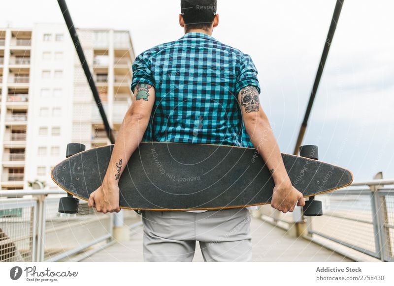 Man with tattoos holding skateboard at shore. Back view. Skateboard Coast Beach Leisure and hobbies Summer Multicoloured youngster Action Youth (Young adults)