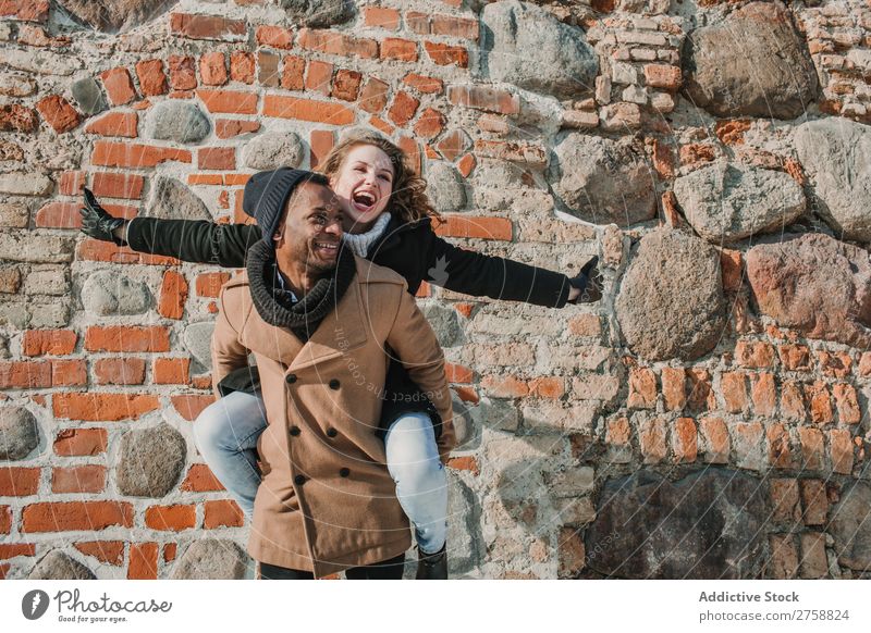 Couple having fun at brick wall multiethnic Style Street warm clothes Easygoing Brick Wall (building) Carrying on back Stone piggyback Beautiful