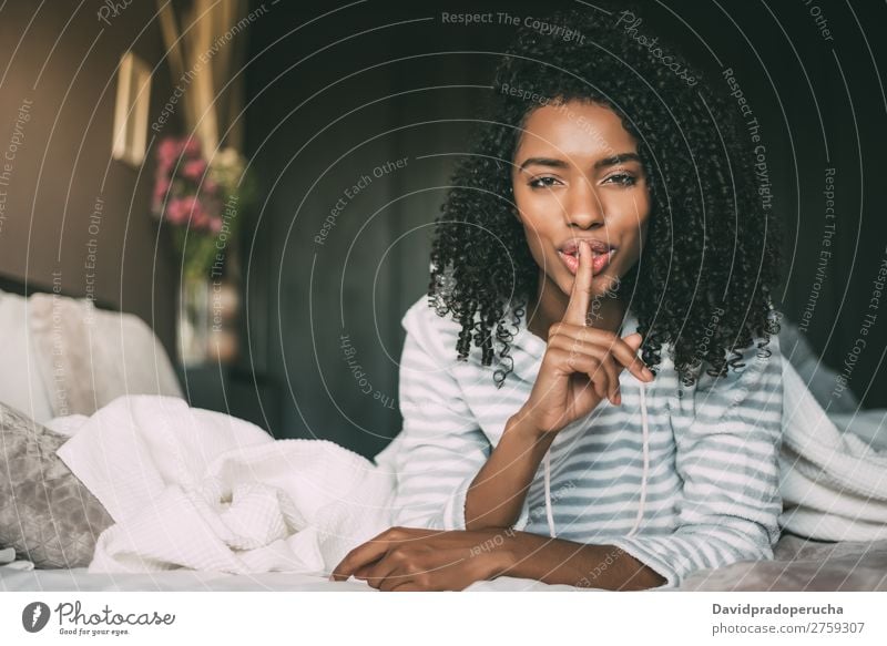 attractive black woman asking for silence with finger on lips on bed Fingers Lips Beautiful Face Mysterious Gesture Woman Bed Portrait photograph Close-up