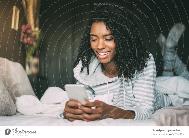 close up of a pretty black woman with curly hair smiling and using phone on bed looking away Woman Bed Portrait photograph Close-up PDA Telephone Mobile