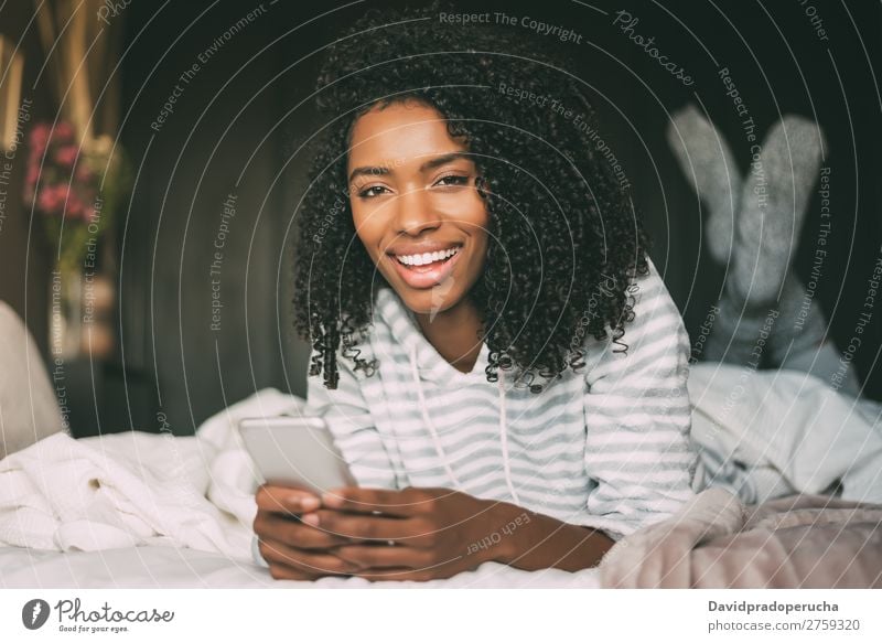 close up of a pretty black woman with curly hair with smartphone on bed looking at the camera Woman Bed PDA Mobile Telephone Portrait photograph Close-up