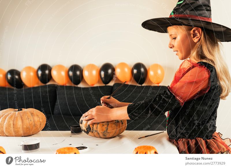 Beautiful girl disguised of witch decorating a pumpkin at home. Hallowe'en Child Girl Painting (action, artwork) Witch Joy Disguised Family & Relations Sister