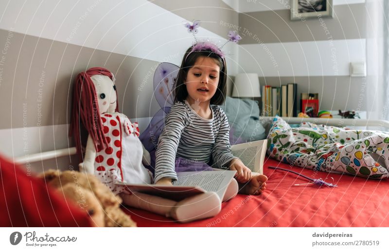Little girl disguised sitting on bed teaching doll to read Lifestyle Beautiful Playing Reading Lamp Bedroom Child Human being Woman Adults Friendship Infancy