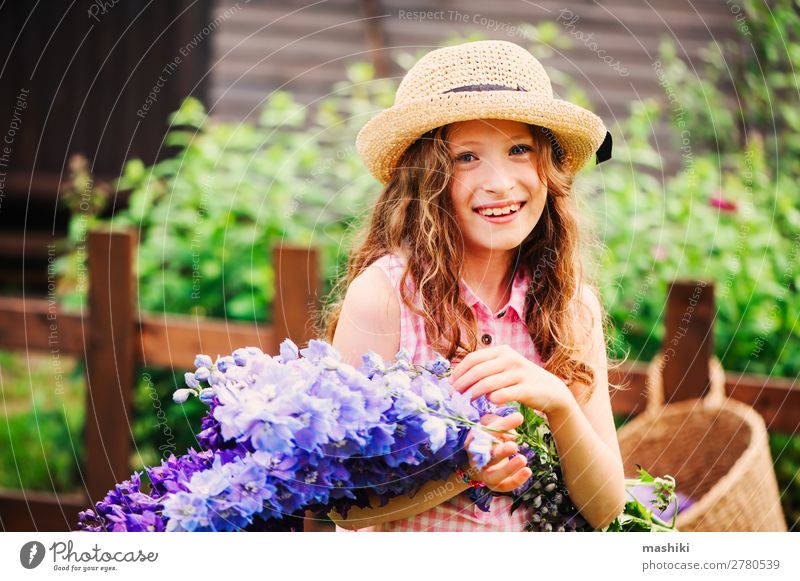 romantic portrait of happy child girl picking bouquet of beautiful blue delphinium flowers from summer garden plant blossom kid play smile funny gardener helper