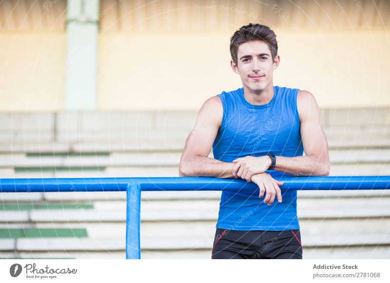 Young man in sportswear leaning on metal fence and posing on sta Man Stadium Athletic Posture Rest sportsman Sports Fitness Contentment Practice Lean Athlete