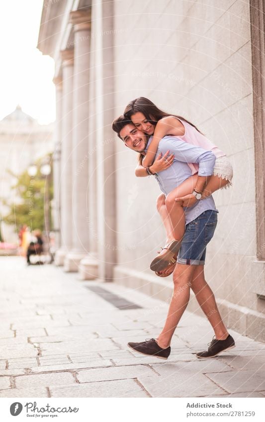 Smiling couple in the street. Couple piggy back Joy Hold Emotions Happy Cheerful Carrying Vertical Day Blur Building Stand Profile Embrace Looking away