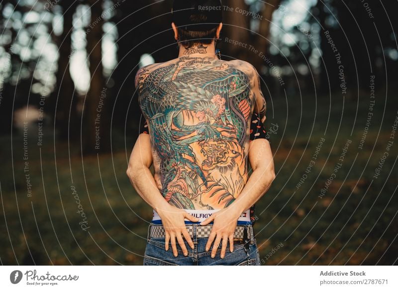 Young guy in tattoos hugging lady in forest Couple Tattoo Embrace Forest snapback Park Lady shirtless Guy Youth (Young adults) Hipster embracing Man Woman