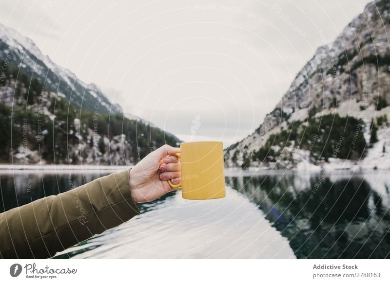 Person with cup near wonderful lake between hills in snow and cloudy sky Human being Lake Hill Snow Sky Pyrenees Clouds Cup Wonderful Mountain Water Surface Mug