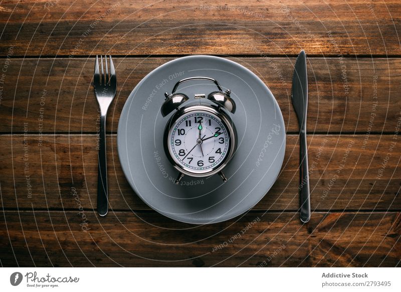 Cutlery near plate with alarm clock Plate Alarm clock Table Conceptual design Diet Fork Knives Time Meal Minute hand Hour hand Lunch Dinner Breakfast Mechanical