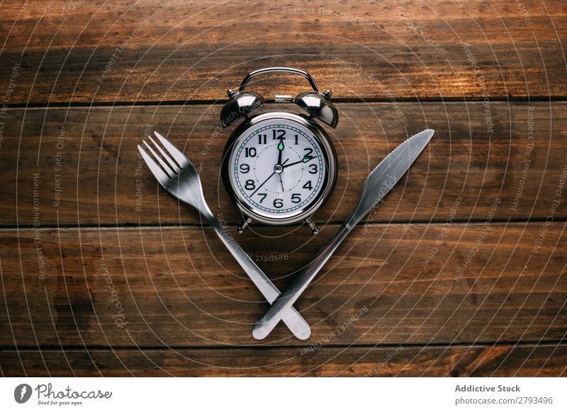 Cutlery near alarm clock Alarm clock Table Conceptual design Diet Fork Knives Time Meal Minute hand Hour hand Lunch Dinner Breakfast Mechanical Metal Style