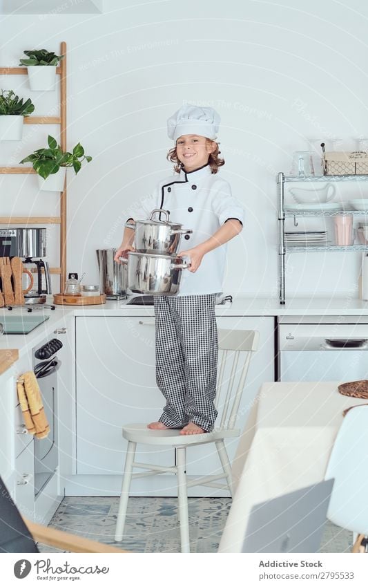 Smiling boy in cook hat holding pots on chair in kitchen Cook Boy (child) Pot Kitchen Chair chef Child Hat Cooking Modern Home Happy Light preparing Happiness