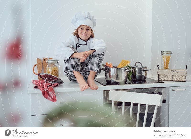 Boy sitting near pots on electric fryer in kitchen Cook Boy (child) Pot Kitchen chef Child Vegetable Hat Stove & Oven Cooking Modern Funny Home Light preparing