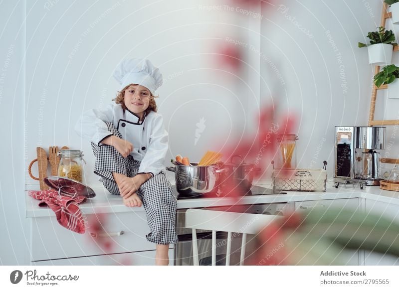 Boy sitting near pots on electric fryer in kitchen Cook Boy (child) Pot Kitchen chef Child Vegetable Hat Stove & Oven Cooking Modern Funny Home Light preparing