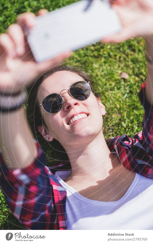 Above view of a young smiling hipster woman lying on grass in a sunny day at a park while taking a selfie with a mobile phone Young woman Hipster Hip & trendy