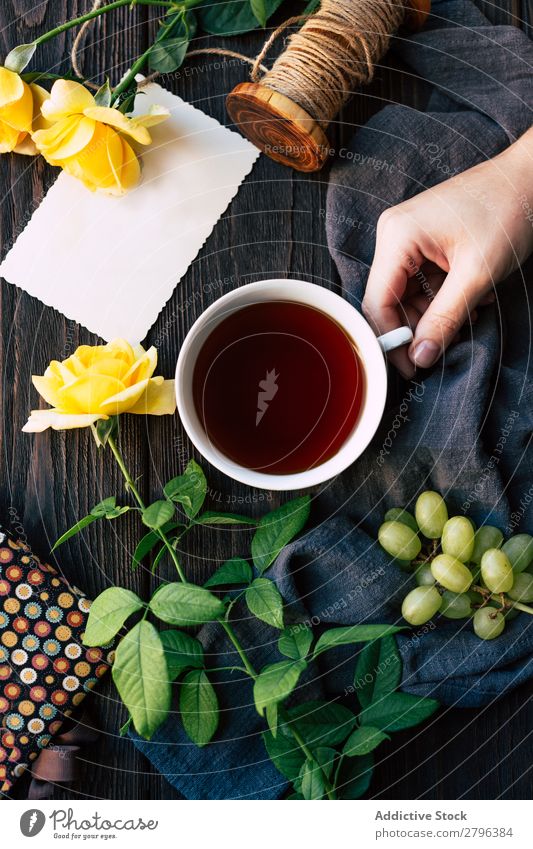 Crop hand with tea near flowers and blank note Hand Rose Tea Blank Table Cloth Bunch of grapes Thread Surprise Gift Cup Drinking Beverage Hot Fresh Flower