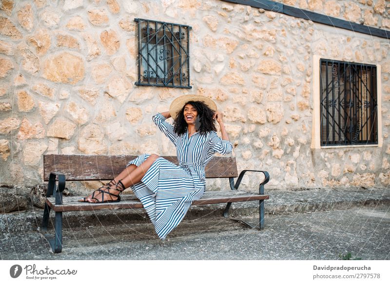 Woman sitting on a bench near a stone house Beauty Photography Close-up Ethnic Black Cheerful Sit Bench African Beautiful Smiling Straw hat Curly hair Happy