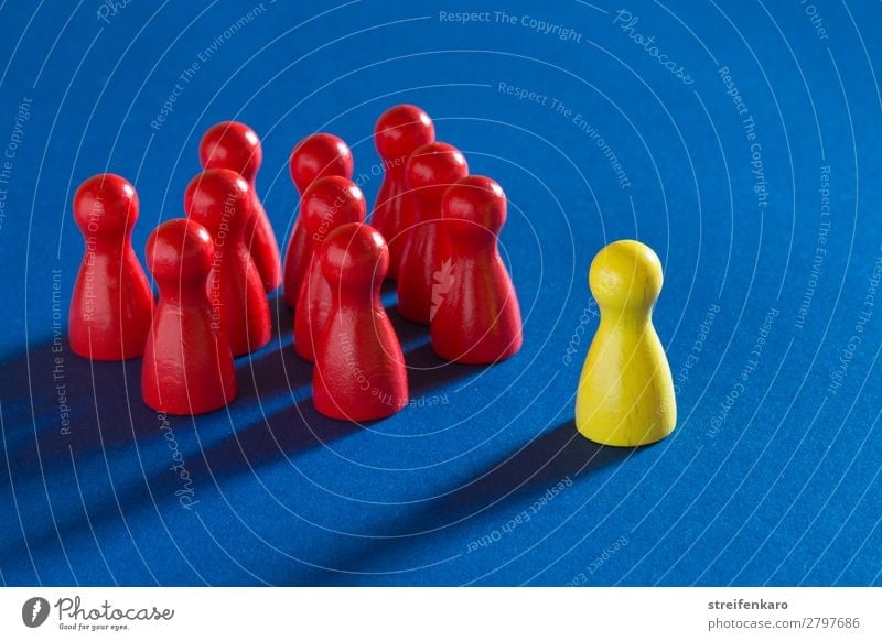 A yellow playing piece stands in front of a group of red playing pieces on a blue background Study Economy Business Career Success To talk Team Group Toys Wood