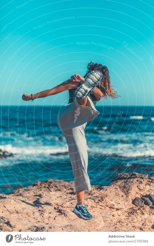 Anonymous female kicking air on seashore Woman Ocean Coast Sky Blue Beautiful weather Lifestyle Leisure and hobbies Waves Stone Water Movement Practice Balance
