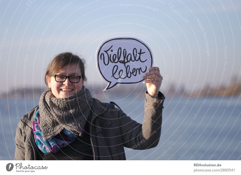 Woman holding speech bubble Living diversity Speech bubble Autumn Jacket Text Words have power variety Smiling Eyeglasses Lake Nature stop To hold on Feminine