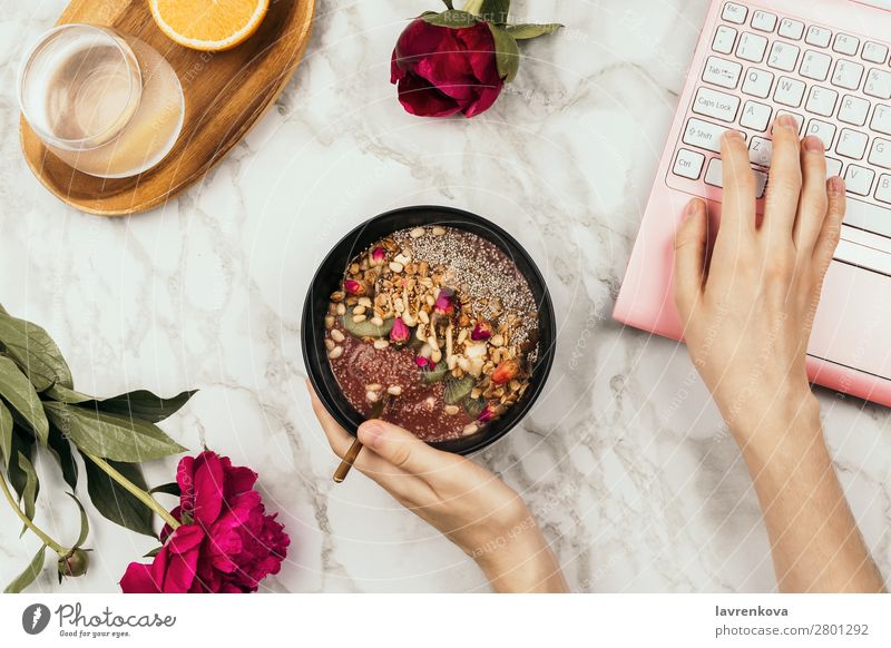 Flatlay of woman's hands holding smoothie bowl with laptop Notebook Orange Water Fruit Milkshake chia pudding Diet Detox Bowl Young woman Snack Meal Morning