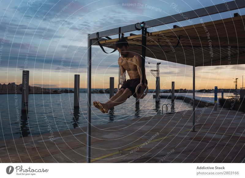Athletic man balancing on gymnastic rings Man sportsman Balance Embankment Ring shirtless Water City Evening Youth (Young adults) upped legs Sports Action
