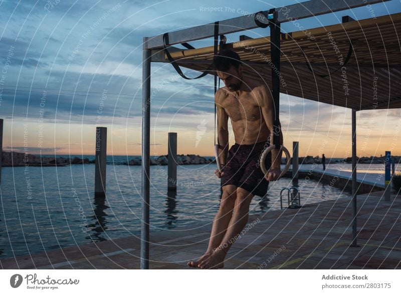 Athletic man balancing on gymnastic rings Man sportsman Balance Embankment Ring shirtless Water City Evening Youth (Young adults) Sports Action workout