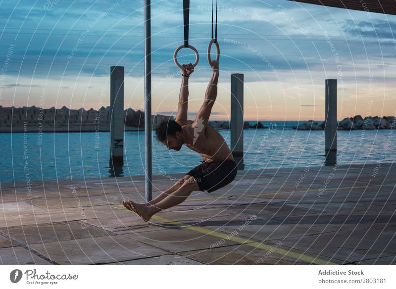 Athletic man balancing on gymnastic rings Man sportsman Balance Embankment Ring shirtless Water City Evening Youth (Young adults) upped legs Sports Action