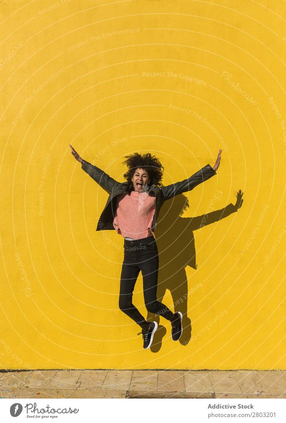 Black woman with afro hair jumping for joy in the street. African Afro American Background picture Beautiful Easygoing Cheerful Colour Energy enjoyment Fashion