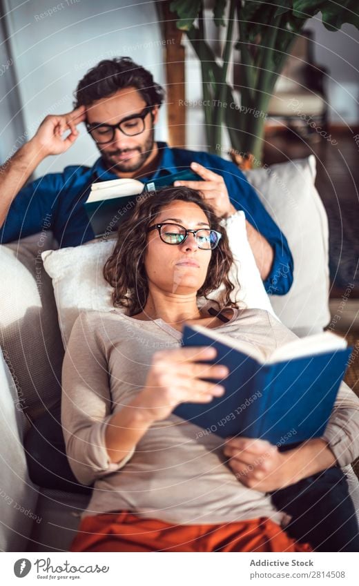 Young couple reading book on couch at home Book Home Literature Sofa Leisure and hobbies closeness Attractive Denim Vantage point Sit Day Life Adults fondness
