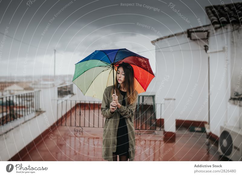 Girl with umbrella against cloudy sky. Woman Stand Hold Multicoloured Rainbow Umbrella Gray Clouds Sky Weather Exterior shot Roof Building Horizontal