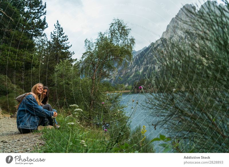Cheerful women sitting at lake Woman Mountain Smiling Sit Together Happy Laughter Hiking Lake Water embracing Vacation & Travel Adventure Tourist