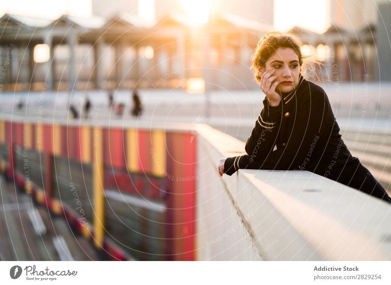 Woman in sunset lights standing at the handrail woman holding head confident looking at camera casual clothes stylish serious young hair female beautiful girl